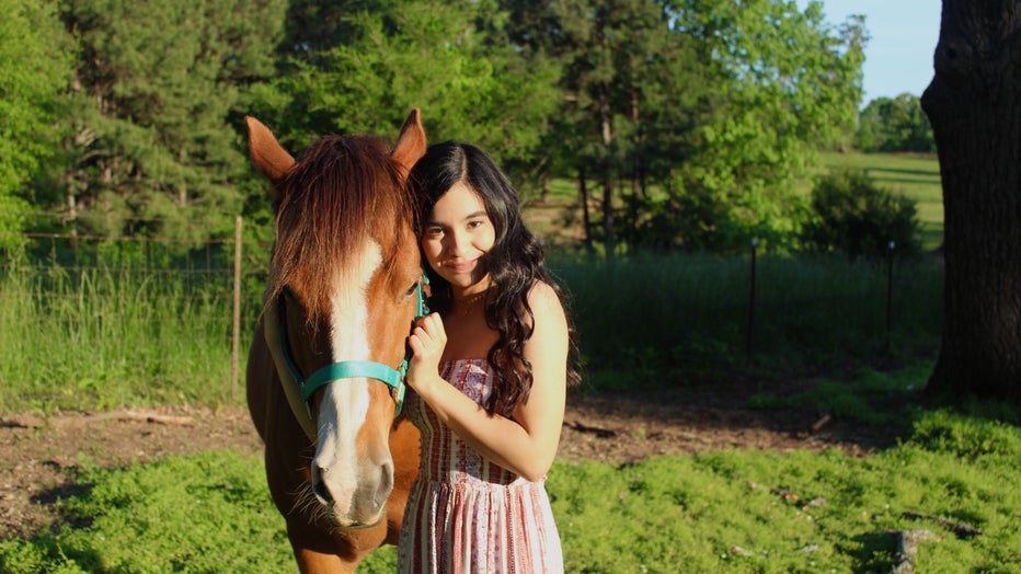 Young woman with long dark hair stands beside a beautiful brown horse