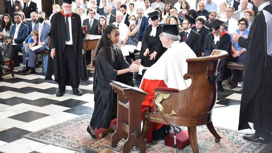 A young African American woman wearing a graduation gown is presented with her master's degree 
