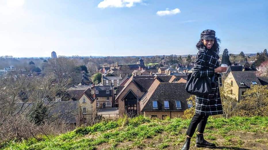 You woman in winter coat stands on hill overlooking the city of Cambridge, England.