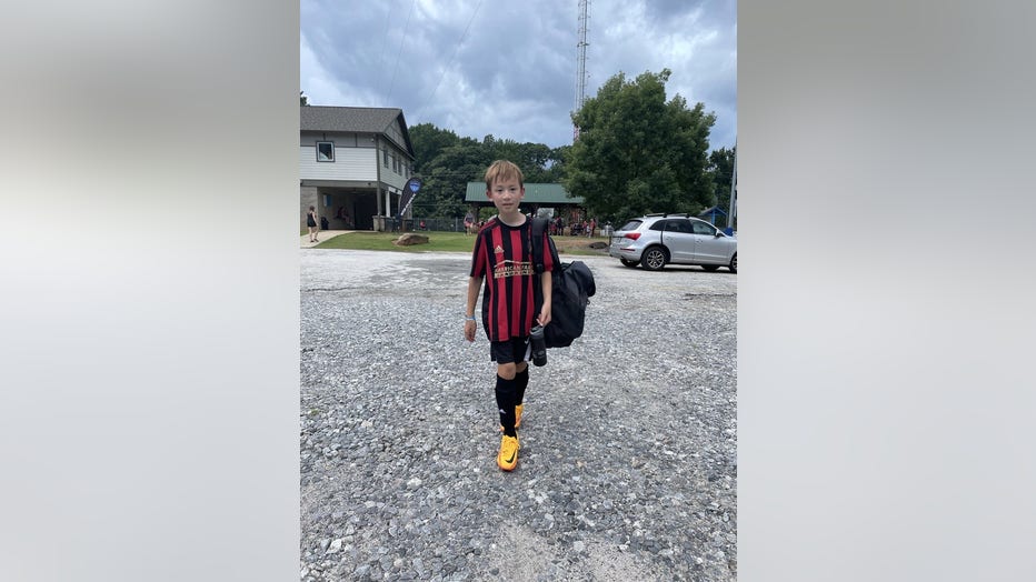 Boy in striped soccer uniform walks across a parking lot.