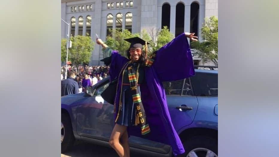 African American girls with long hair poses in her graduation gown, her hands raised up in the air.