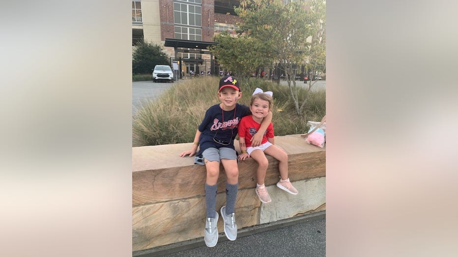 Little boy wearing Atlanta Braves hat and shirt hugs his younger sister.