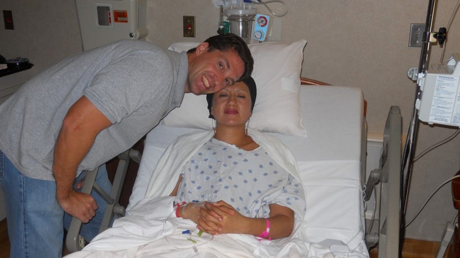 Husband stands over the hospital bed where his wife is sitting