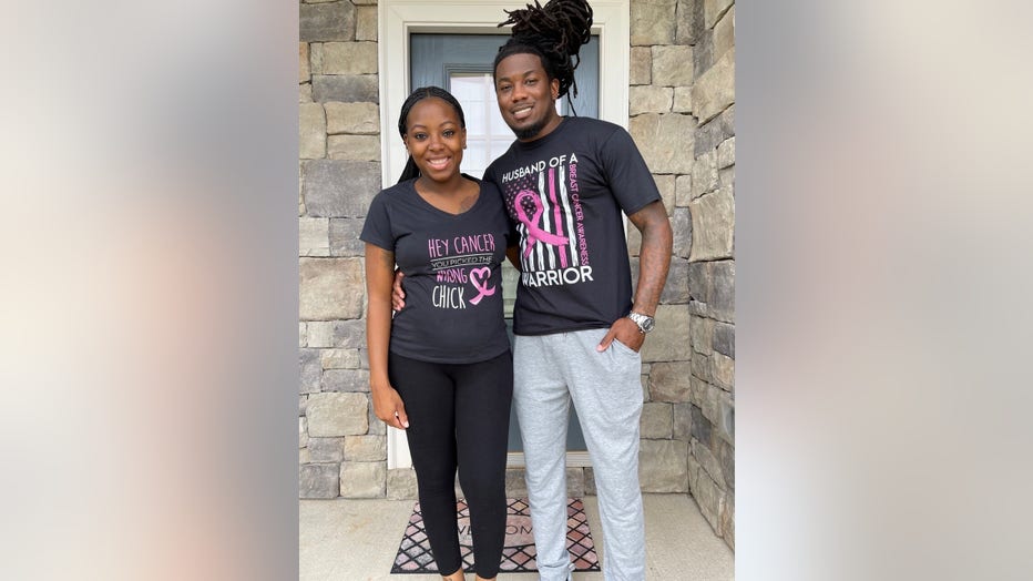 April and her husband Leo stand on their front porch. They're wearing breast cancer awareness t-shirts and have their arms around each other.