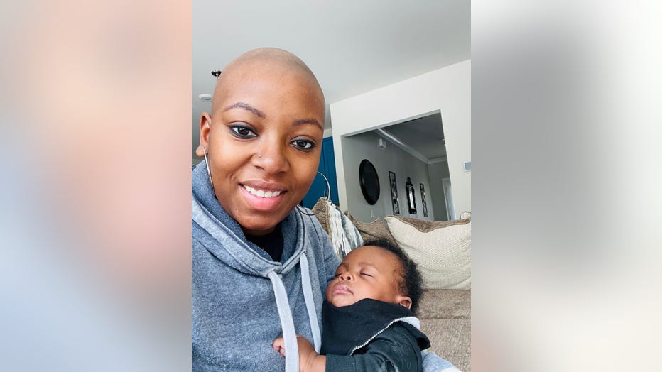 A young Black woman with a bald head holds her newborn son and smiles. At the time, she was going through 4 months of chemotherapy. 