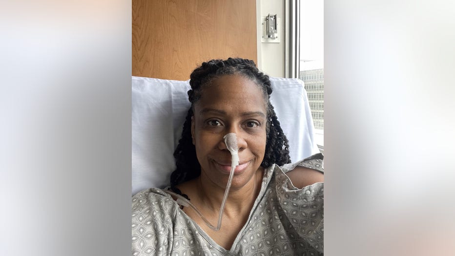 Woman wearing a nasal feeding tube smiles as she sits in her hospital room. She looks peaceful.