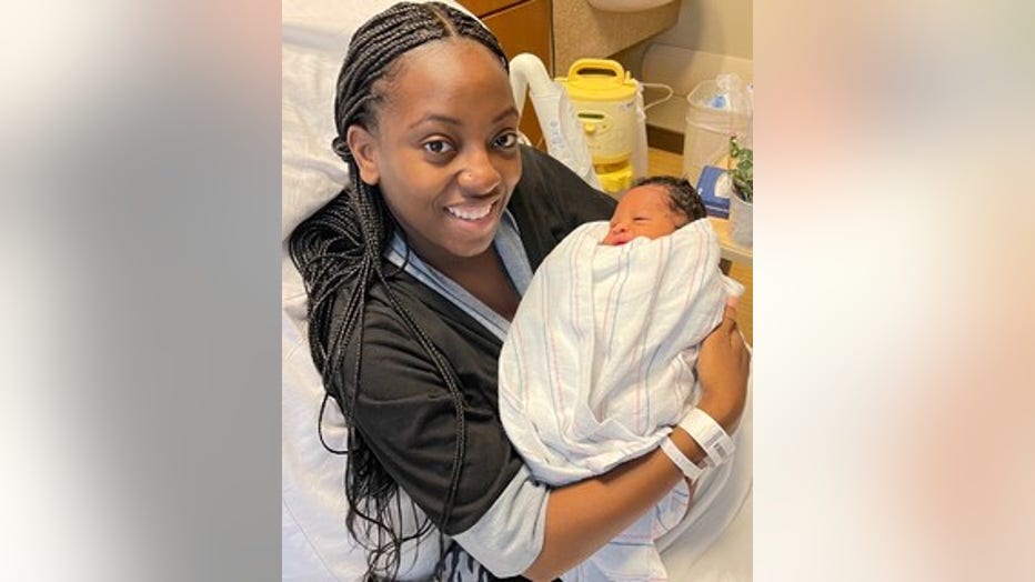 A young Black woman holds her newborn son in her arms in a hospital bed. She is smiling.