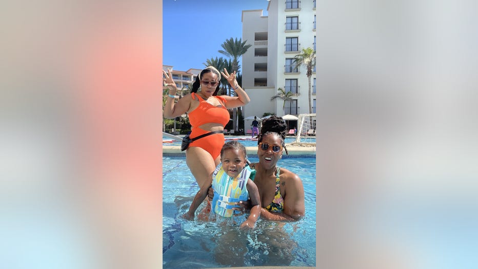 Two women pose in the pool with their young son.