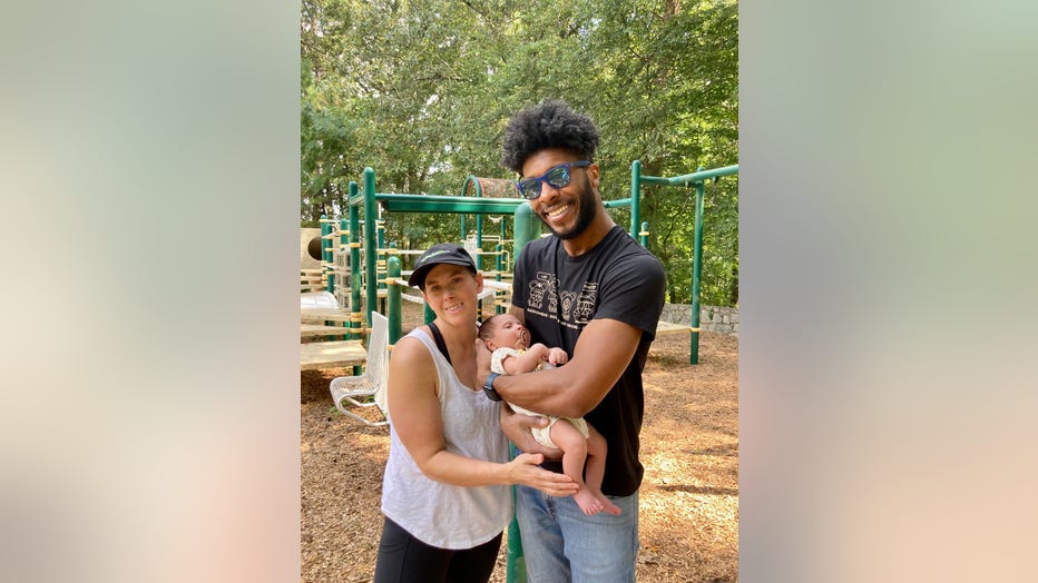 A couple holding a baby pose for a photo on a playground
