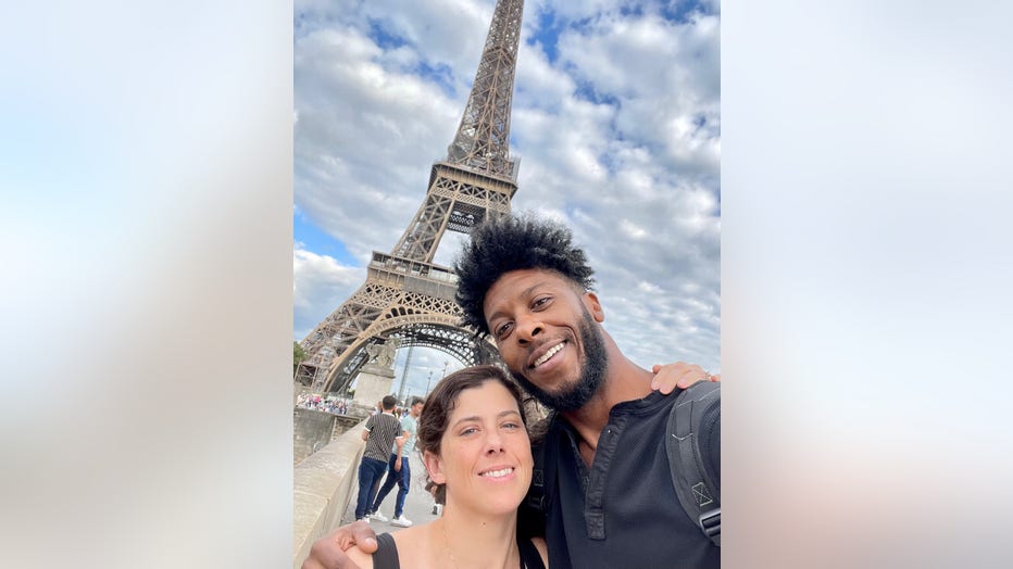 A couple hugs while taking a selfie in front of the Eiffel Tower