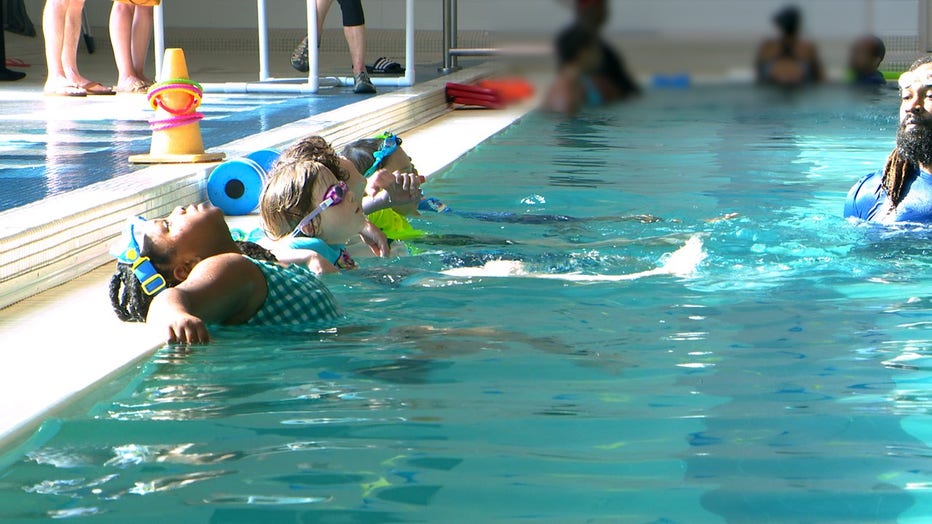 Young African American girl stretches back along the side of a swimming pool during a break from her swimming lessons at the YMCA.