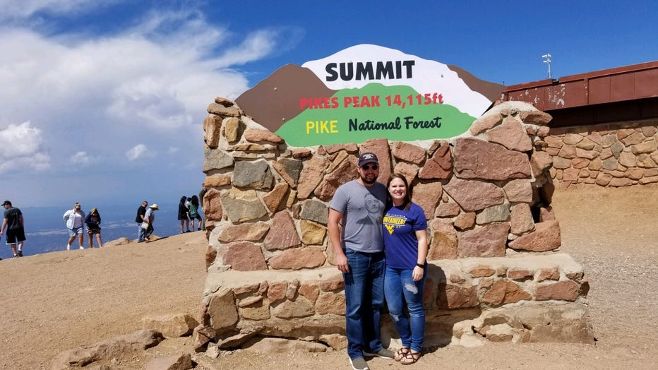 Couple poses in from of a stone sign that reads "Pikes Peak"