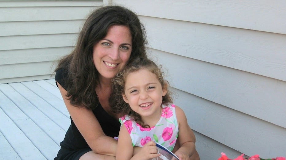 A woman hugs her 4-year-old daugher, who has long cur;ly hair, as they sit outside on a porch, both of them smiling.