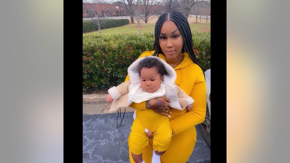 A Black woman with long hair sits outside with her newborn in her lap. They're wearing matching yellow outfits and she is smiling.