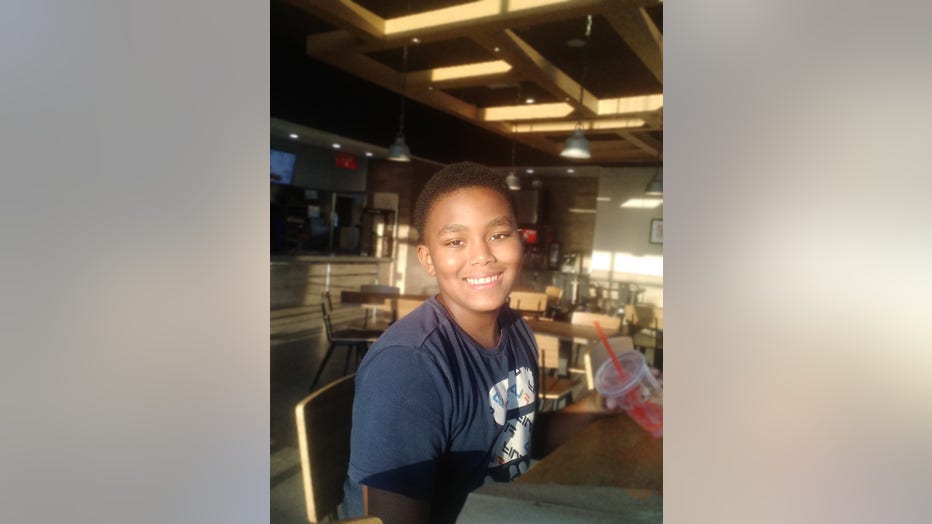 12-year old boy sits at a table and smiles at the camera.