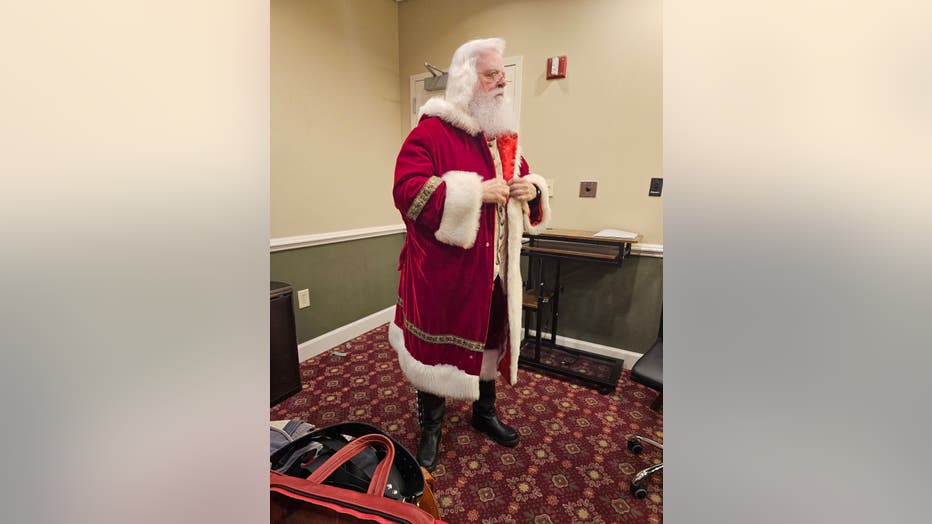 A very realistic looking Santa Claus adjusts his heavy red jacket as he prepares for an appearance.