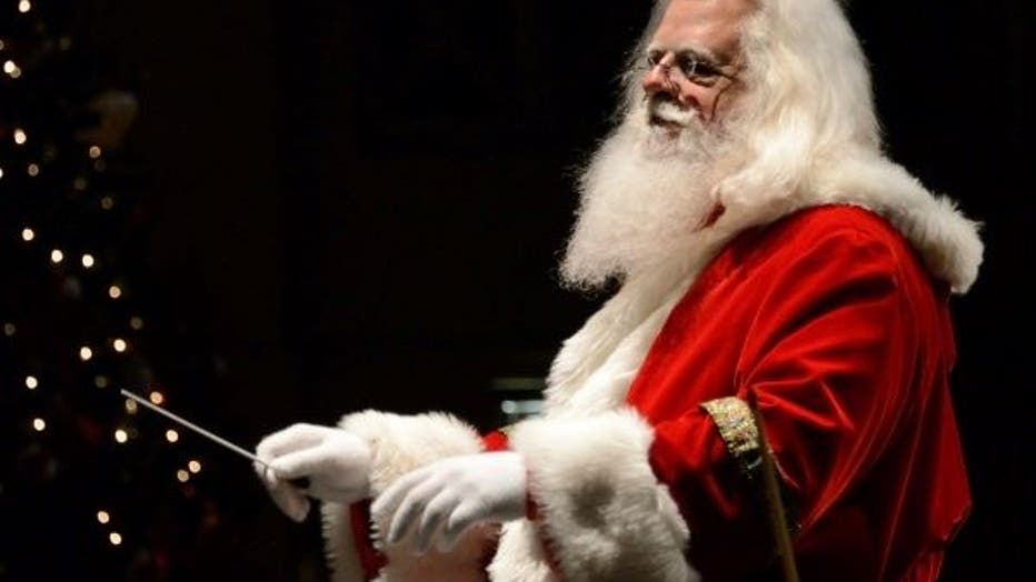 A very realistic looking Santa Claus pretends to lead the Athens Symphony Orchestra against the backdrop of a sparkling Christmas tree.