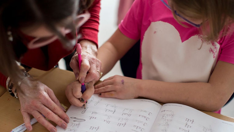 FILE - A teacher helps her third grade student with the placement of her hand while writing the letter "f" in cursive at Narragansett Elementary School on Dec. 20, 2018. (Staff photo by Brianna Soukup/Portland Portland Press Herald via Getty Images)