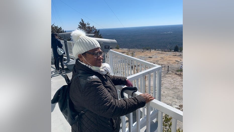 A Black woman in a winter hat and coat stands on an overlook, looking off in the distance.