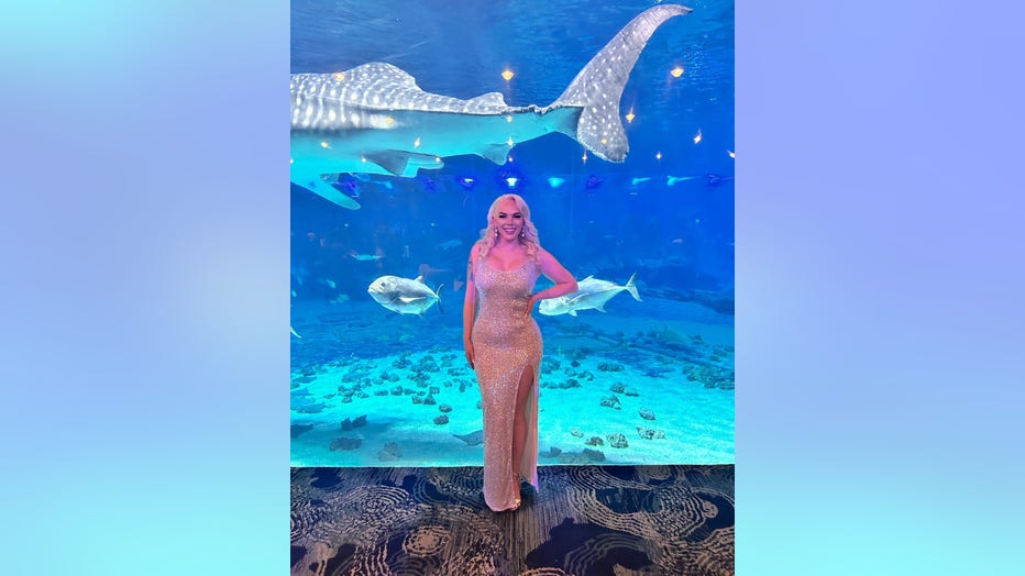 Young woman in party dress stands in front of a shark tank at the Georgia Aquarium.