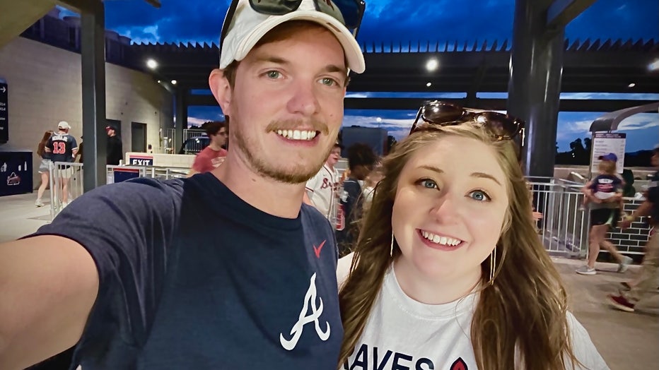 A couple wearing Atlanta Braves shirts pose for a selfie photograph.