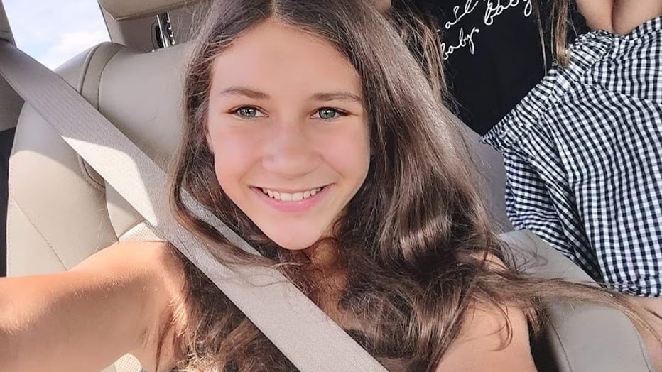 A 13-year-old girl sitting in a car smiles as she takes a selfie.