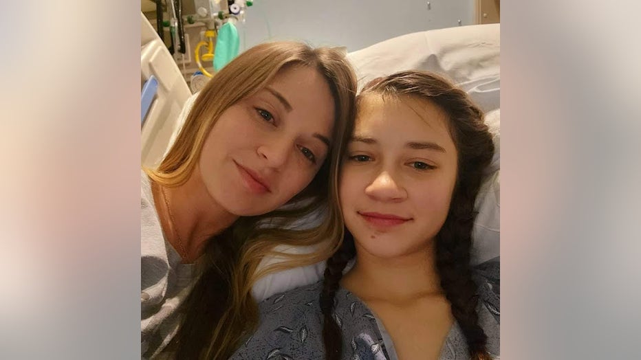 Mother and teen daughter pose for a photo from the girl's hospital bed.