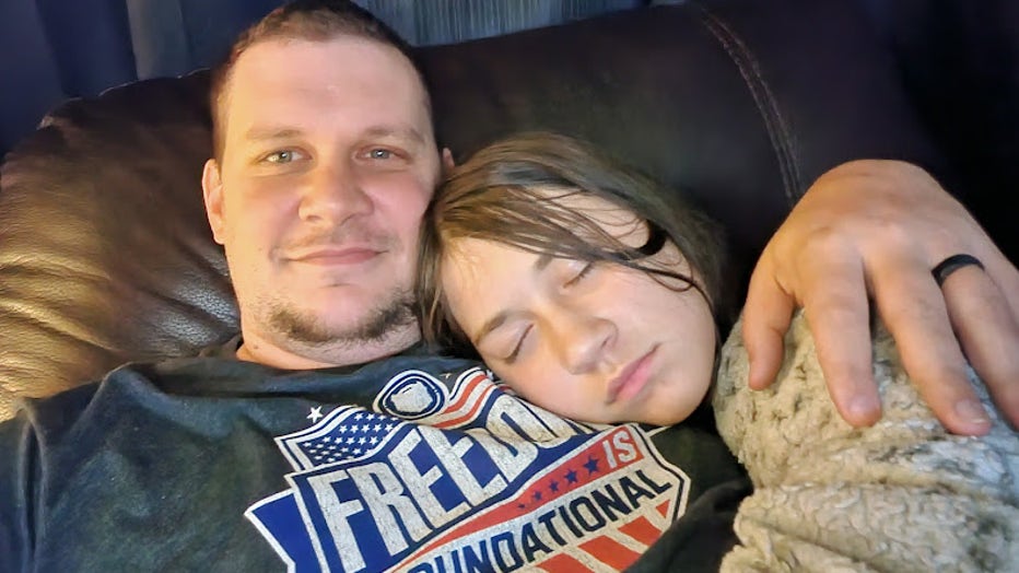 A father takes a selfie with his daughter resting her head, her eyes closed, on his shoulder.