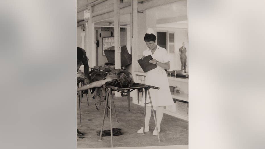 Woman in nurse whites holds a clipboard in the triage hospital of her Vietnam field hospital.