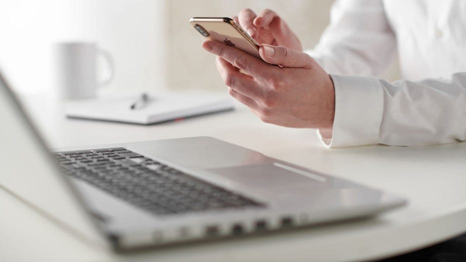 FILE - Close up detail of a business person working at a desk with a smartphone and laptop computer, taken on January 31, 2019. (Photo by Neil Godwin/Future via Getty Images)