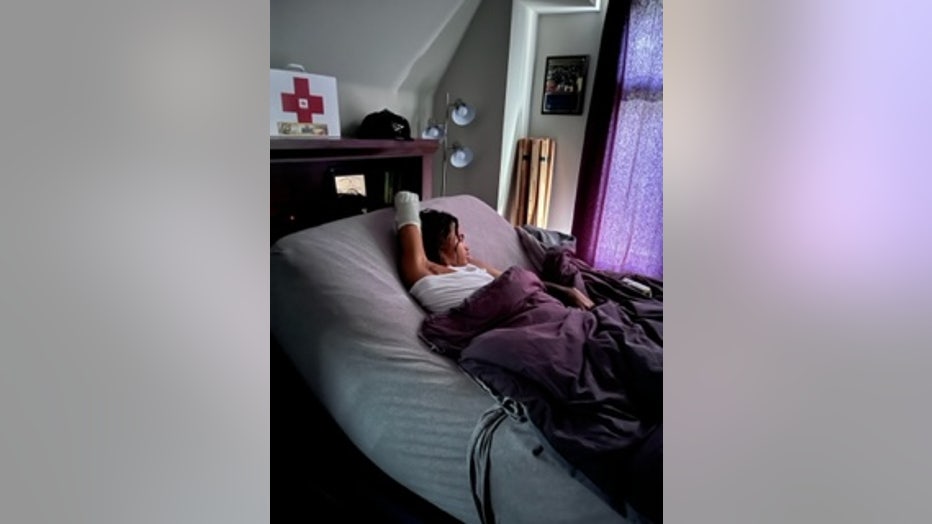 A young man sits in bed at home, with the lights turned down low.
