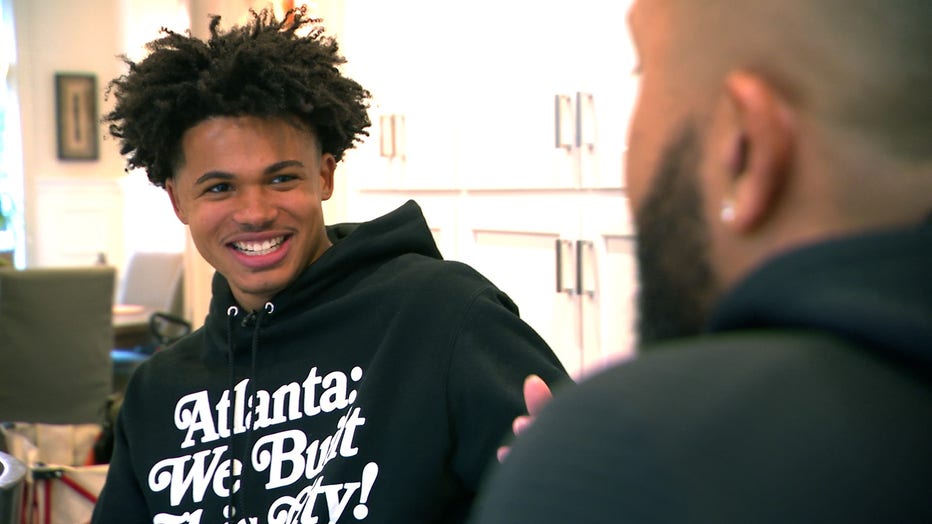 A teenage boy smiles as he listens to someone talking.