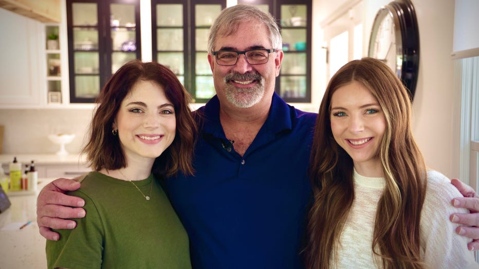 At 53 year old father stands between his two twenty-something daughters.