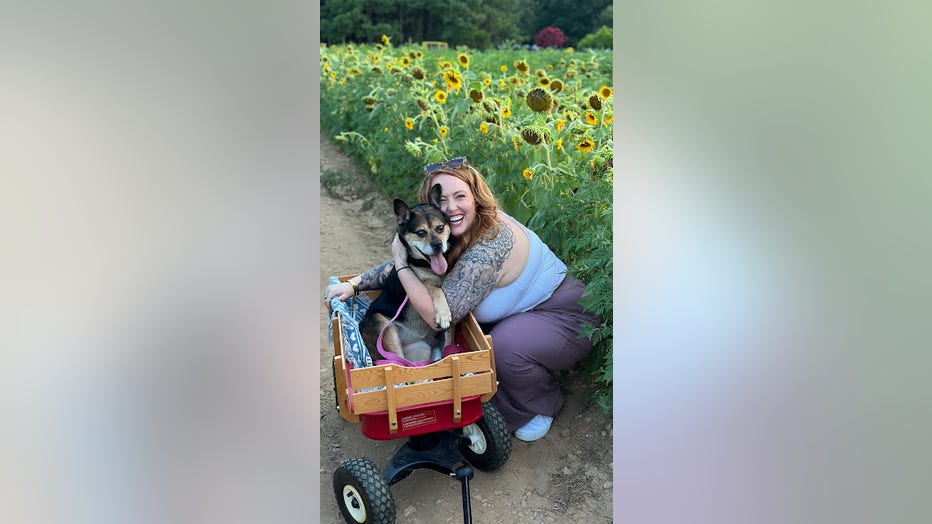 A woman hugs her dog, who is sitting in a wooden wagon.