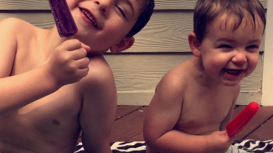 Two boys, then about 6 and 3, smile and hold up popsicles after going swimming.