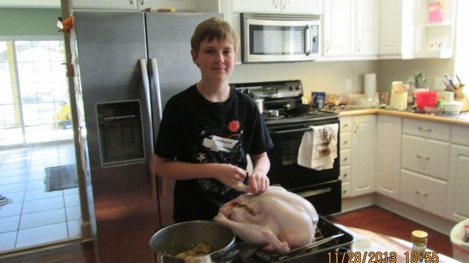 A teenage boy stands in the kitchen next to a Thanksgiving turkey.