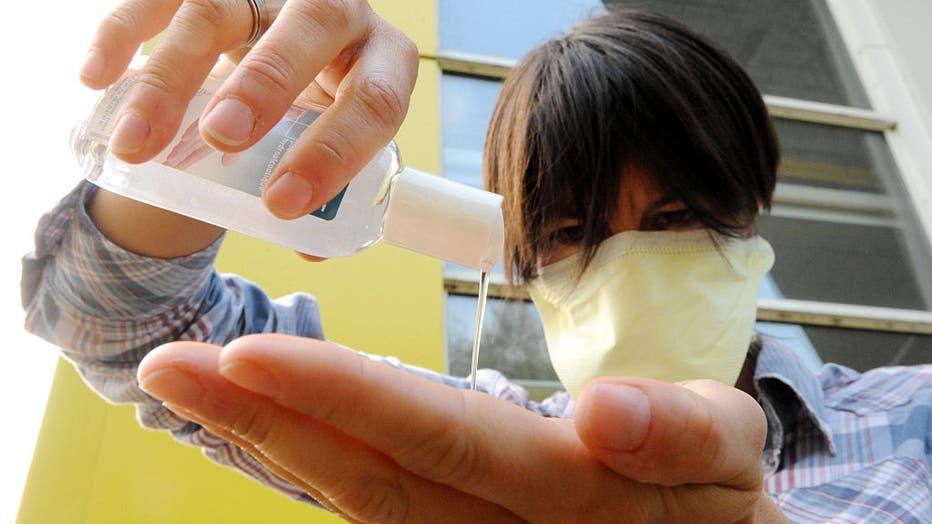 FILE - A woman wearing a surgical mask uses hand sanitizer.