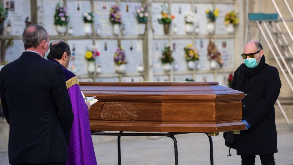 A man wearing a face mask stands by the coffin of his mother during a funeral service in the closed cemetery of Seriate, near Bergamo, Lombardy, on March 20, 2020 during the country's lockdown aimed at stopping the spread of the COVID-19 pandemic.