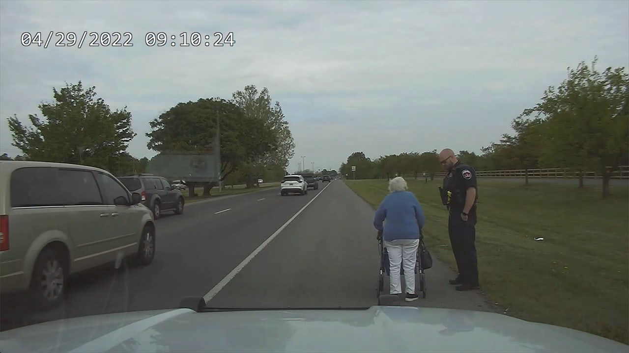 Officer escorts elderly woman walking along busy highway to hair salon