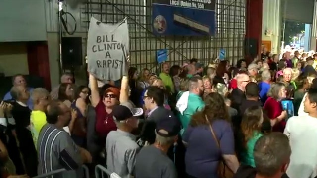 Protester holds 'Bill Clinton a rapist' T-shirt at rally