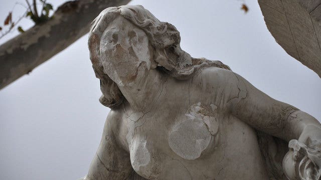 Man with hammer hacks statue of bare-breasted woman