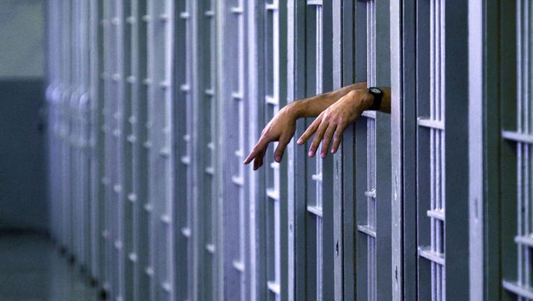 An inmate's hands peer out from inside a jail cell