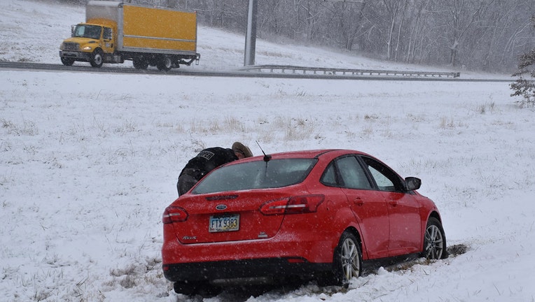 A red car stuck in the snow on the side of a highway