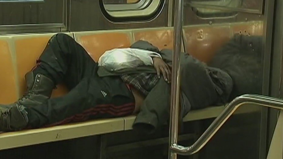 An indigent person sleeping on some seats in a subway car