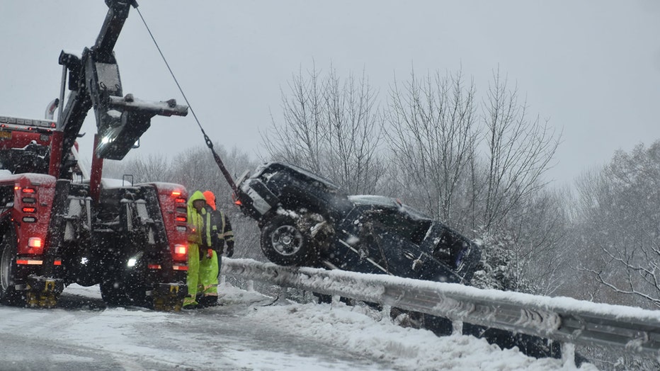 An emergency vehicle lifts a truck out of a ditch off the side of a highway