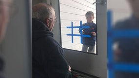 Boy plays Tic-Tac-Toe with grandpa through glass door while practicing 'social distancing'