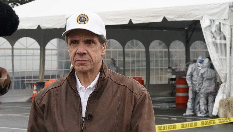 Gov. Andrew Cuomo iun a white cap stands outside a large testing tent