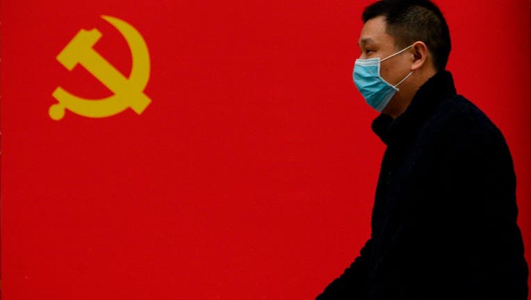 A man wearing a face mask as a preventive measure against the COVID-19 coronavirus walks past a Communist Party flag along a street in Wuhan in China's central Hubei province on March 31, 2020.