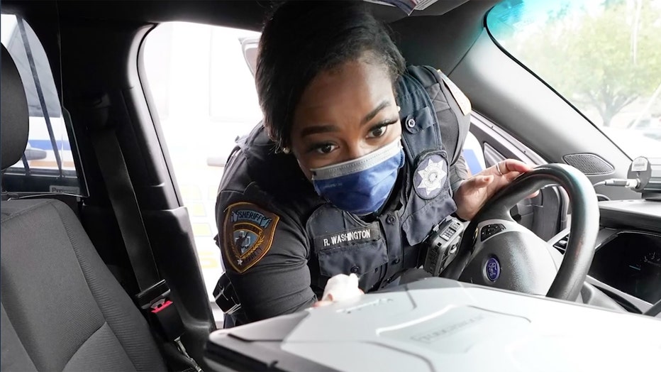 A sheriff's deputy wears a mask and wipes down the inside of her car