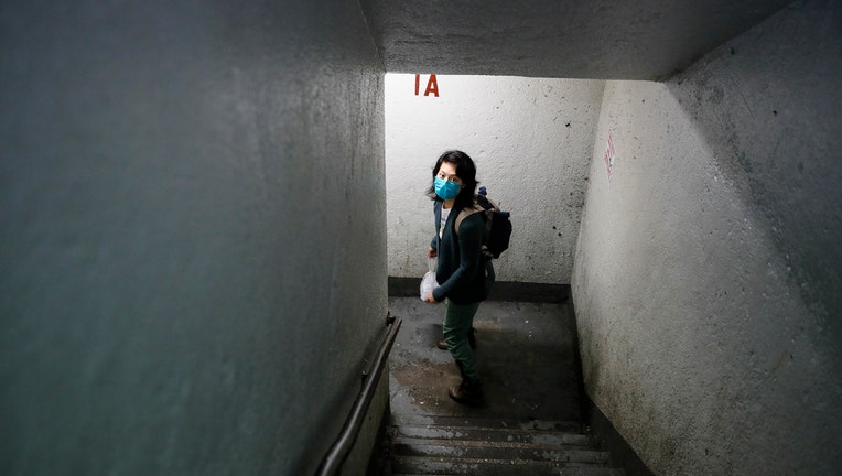 A woman, Dr. Jeanie Tse, wearing a mask, walks down a stairwell